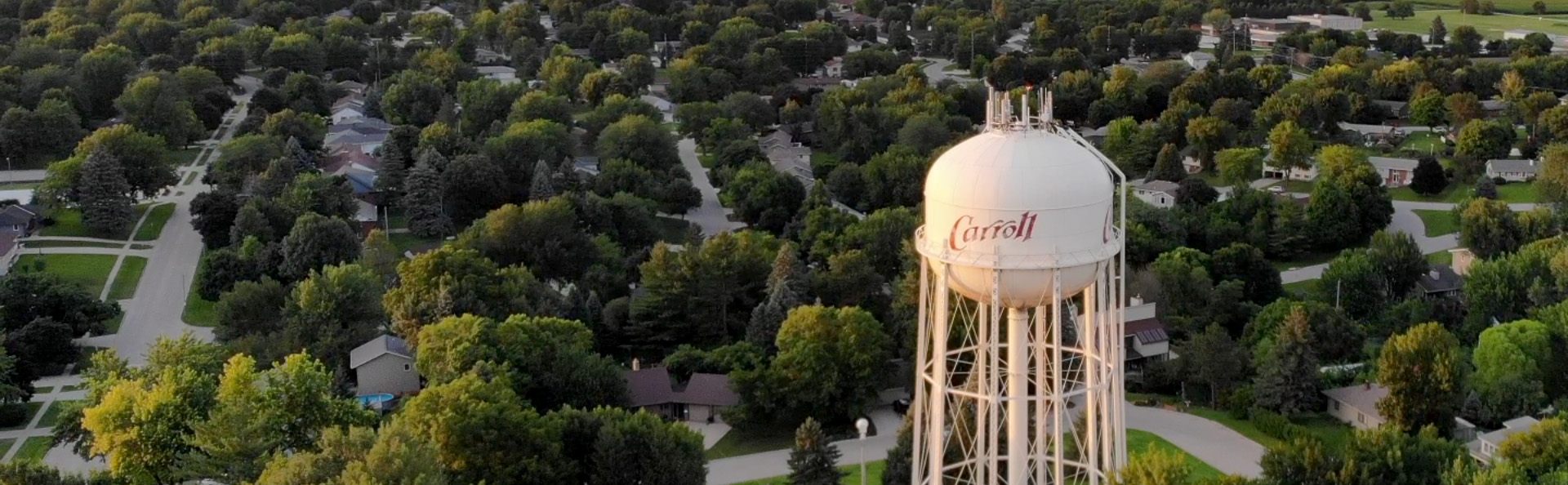Aerial view of Carroll, Iowa at golden hour, showing tree-lined residential streets around the municipal water tower.